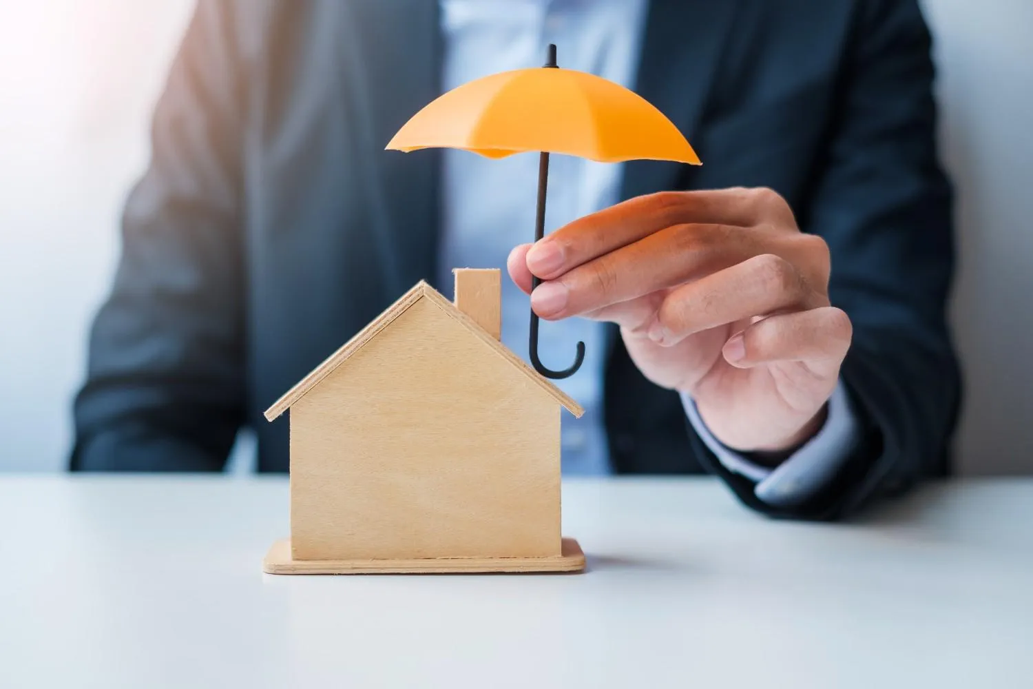Umbrella held over a small wooden house model