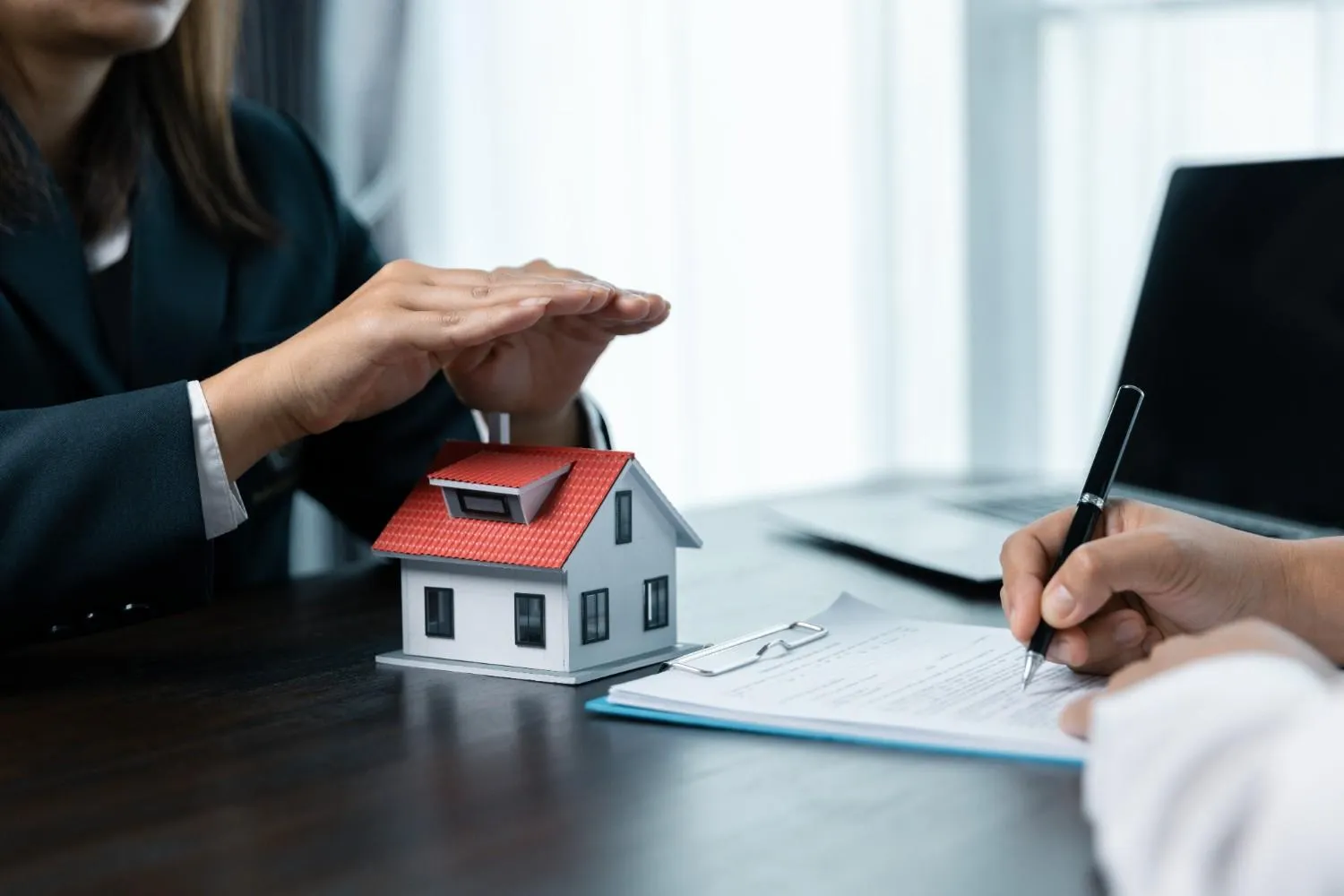 Hand sheltering a house model while a home policy is signed